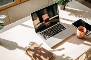Ein Laptop steht auf einem sonnigen Arbeitsplatz, daneben liegt ein Tablett und eine Teetasse.