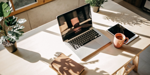 Ein Laptop steht auf einem sonnigen Arbeitsplatz, daneben liegt ein Tablett und eine Teetasse.