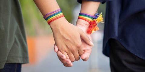 Hände von LGBT-Personen, die Händchen halten und Armband mit Regenbogenfarben tragen