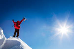 Person steht auf einem schneebedeckten Berg vor blauem Himmel.