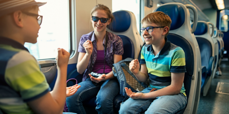 3 Kinder sitzen im Zug und spielen mit den Händen und lachen. 
