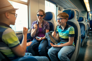 3 Kinder sitzen im Zug und spielen mit den Händen und lachen. 