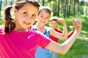 Drei Kinder stehen hintereinander, zeigen mit ihren linken Armen (Muskel)Kraft und Stärke.  