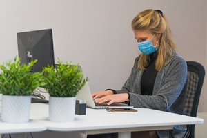 Junge Frau trägt Mund-Nasen-Schutz und arbeitet am PC