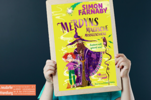 Kind hält eine Tafel mit Cover des Buches: Merdyns magische Missgeschicke