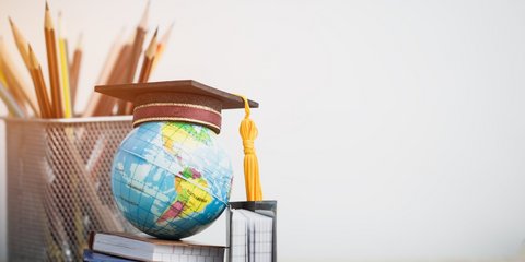 Absolventenkappe auf Modellkugel und Bücher mit Stiften auf weißem Holzhintergrund