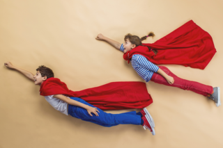 Ein Bub und ein Mädchen, verkleidet als Supermen, fliegen durch die Welt.