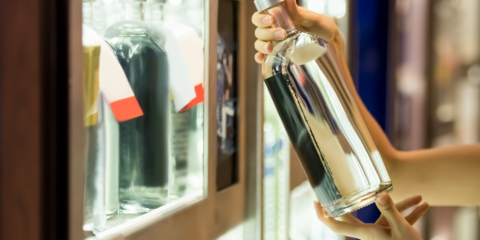 Jugendliche:r nimmt Flasche Alkohol aus der Vitrine im Geschäft. 