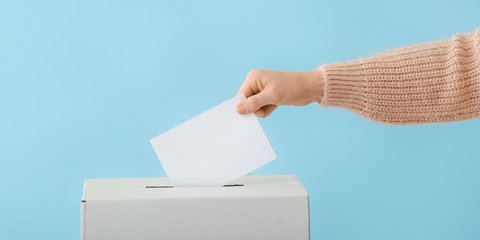 Person gibt Stimmzettel in Wahlurne