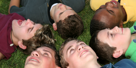 Eine Gruppe Jungs liegt in der Wiese mit den Blicken zum Himmel