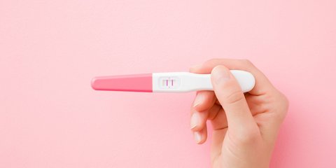 Hand einer jungen Frau mit positiven Schwangerschaftstest auf pastellrosa Hintergrund