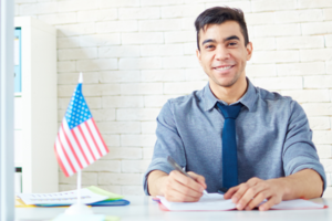 Ein junger Mann mit Hemd und Krawatte sitzt an einem Schreibtisch neben einer Fahne
