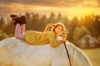Mädchen - als Pippi Langstrumpf verkleidet - liegt auf dem Rücken eines Pferdes